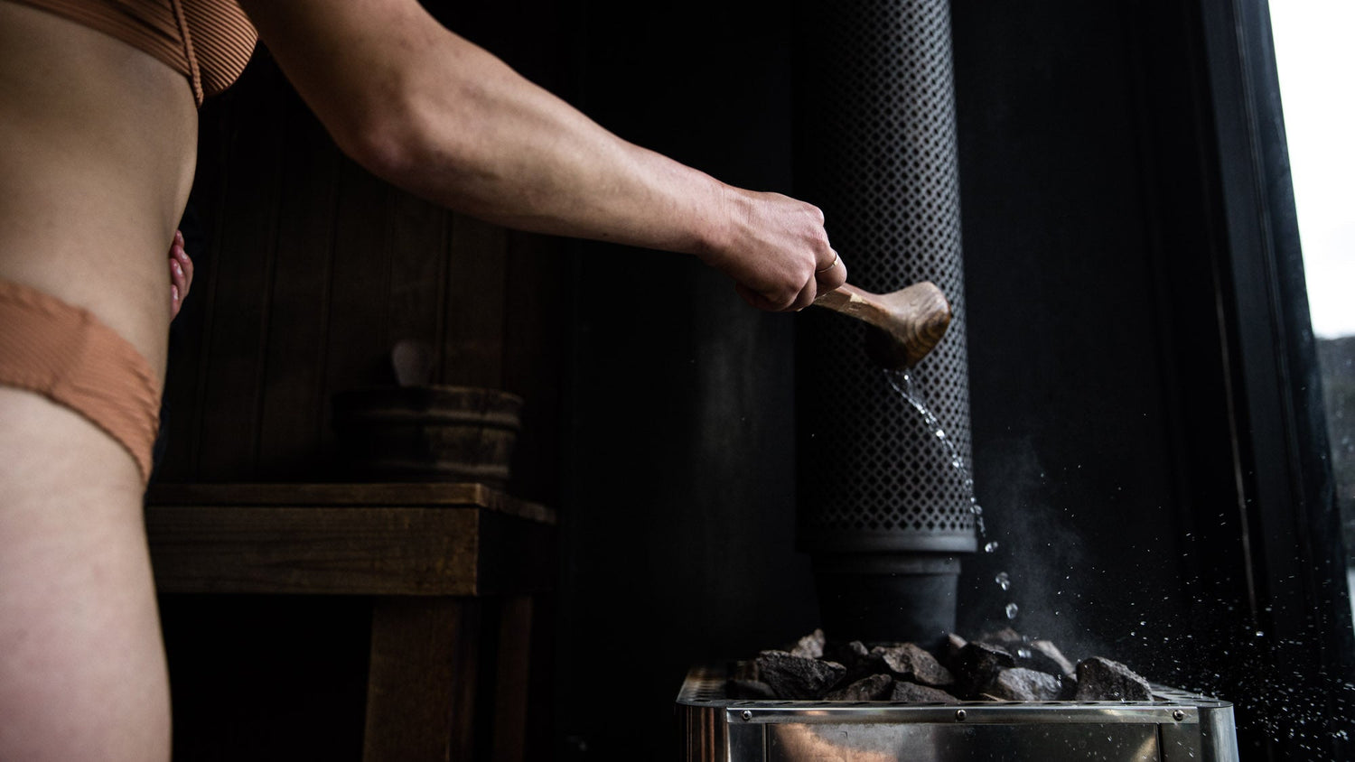 Person using a wooden tool to stir coals in a metal container with a dark background
