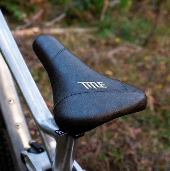 Close-up of a bicycle seat with 'title' branding on a blurred natural background
