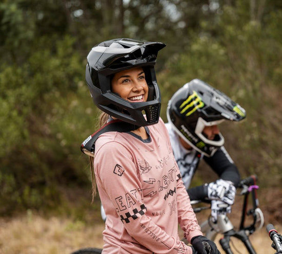 Person wearing a pink jersey and black helmet with a blurred background of other riders on bikes.